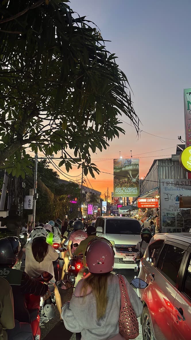 Scooter and car traffic on a Canggu main road under an orange sunset sky