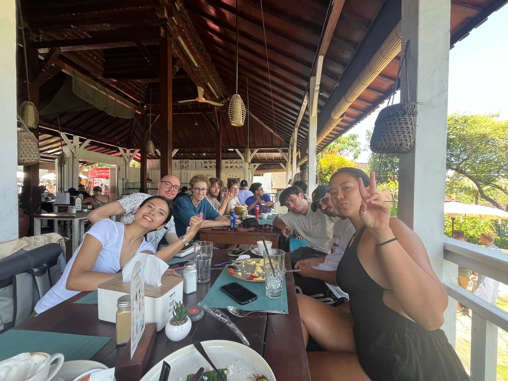 Students sharing breakfast around a long table at an open-air warung in Bali
