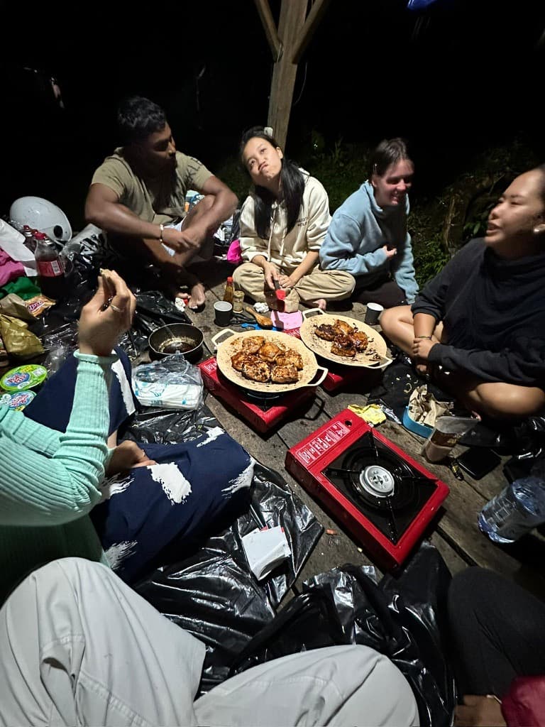 The group sitting in a circle around shared plates of grilled chicken at camp