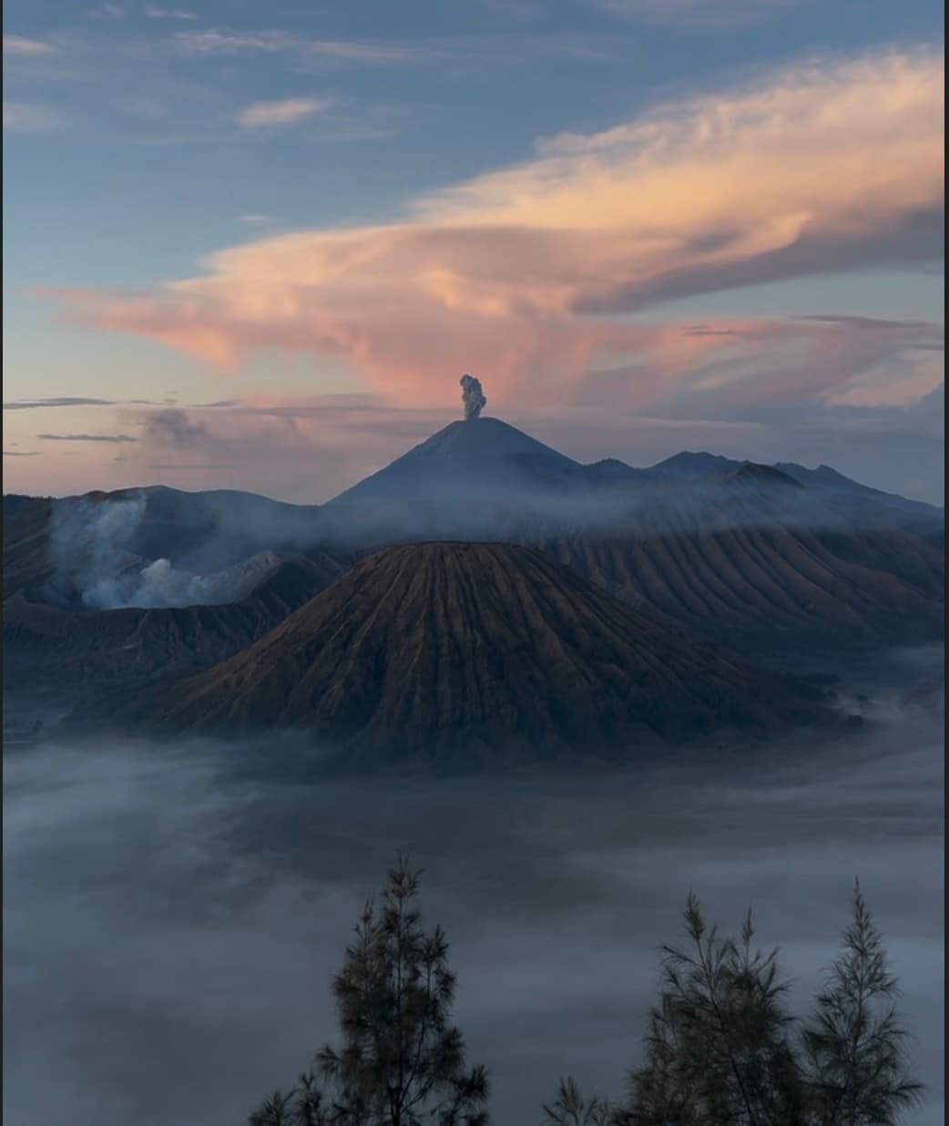 A volcano at sunrise with a plume of smoke rising above a sea of morning cloud
