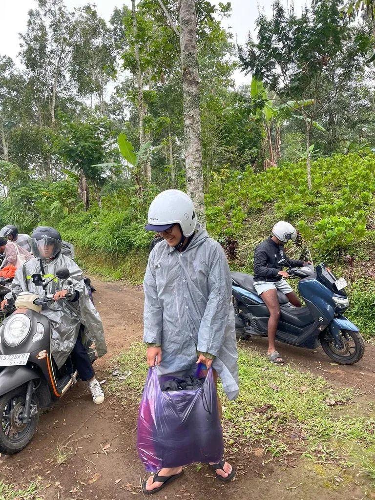 Interns in rain ponchos stopped beside their scooters on a wet track in the Bali highlands